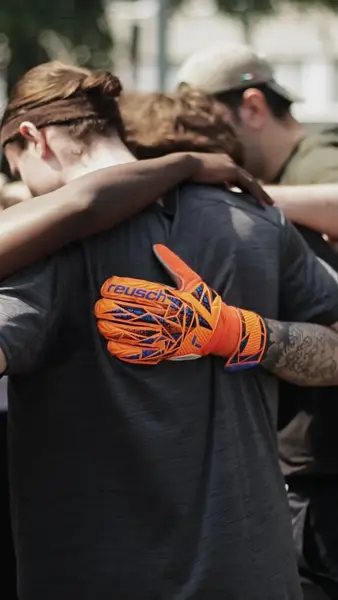Goalkeeper with an orange glove hugging teammates in a huddle