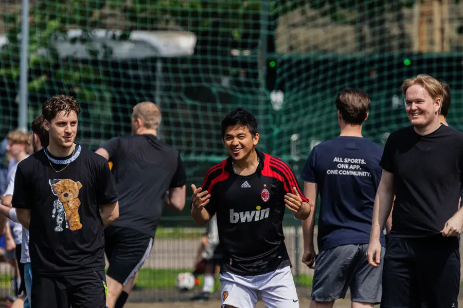 Laughing player in an AC Milan shirt walking with teammates on a sunny pitch